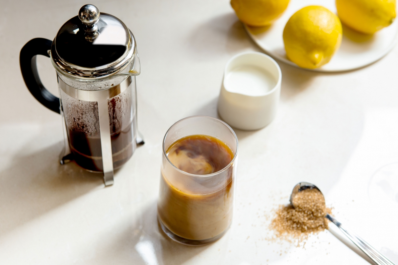 Pöydällä kahvin valmistukseen tarvittavat välineet: pressopannu, maitokannu, kahvimuki ja lusikallinen sokeria.